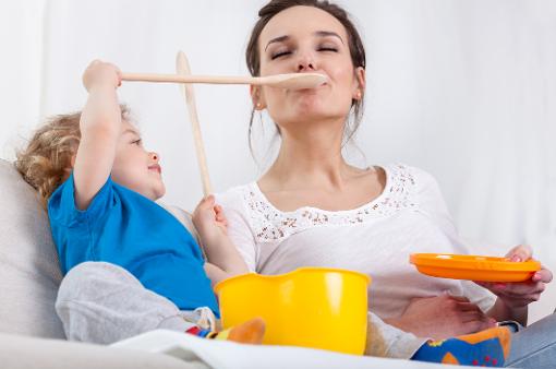 child playing with mum, pretending to feed her with a wooden spoon